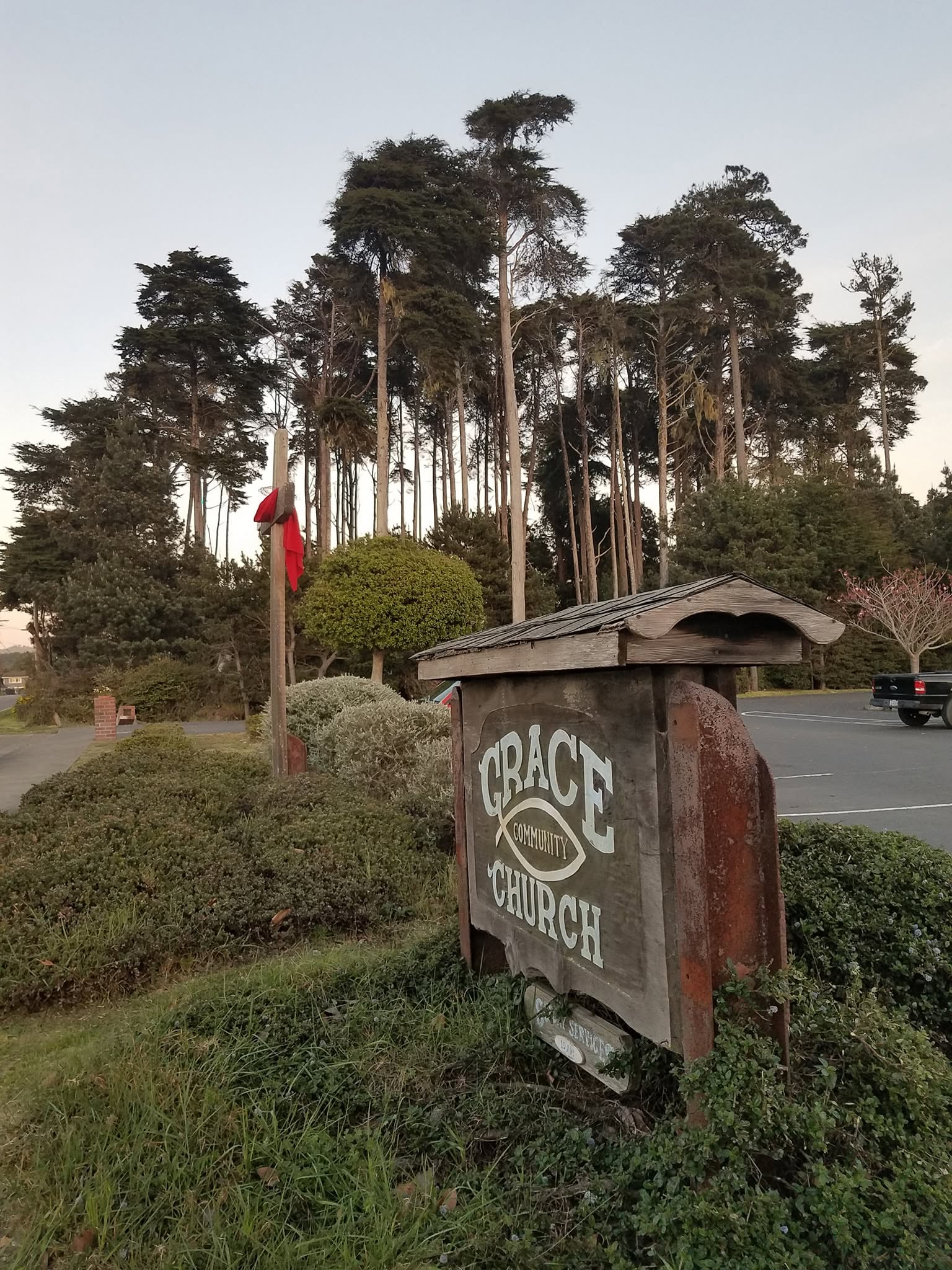 Wooden Grace Community Church sign with cypress trees behind it